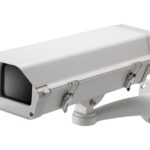 Überwachungskamera an einer Wandhalterung in einem weißen Gehäuse.