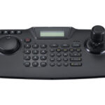 Ein schwarzes Steuerungspult mit einem Joystick, einer Wählscheibe, numerischen Tasten und einem Display.