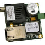 Elektronische Leiterplatte mit verschiedenen Komponenten, darunter ein RJ-45-Anschluss, ein zylindrischer Kondensator und ein BNC-Stecker.