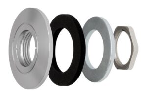 Einzelteile einer mechanischen Vorrichtung: Vier Teile, darunter eine silberne Metallkappe, eine schwarze Dichtung, eine graue Unterlegscheibe und eine sechseckige Mutter.