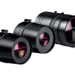 Drei schwarze Kameraobjektive in verschiedenen Größen, die nebeneinander liegen, mit sichtbaren Einstellringen und violett getönten Linsen.