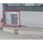 Eine Person verlässt ein Gebäude durch eine Tür auf einer erhöhten Plattform, umgeben von roten Umrisslinien.