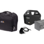 Eine schwarze Tragetasche mit dem Logo „AXIS Communications“, ein schwarzes tragbares Gerät mit Griff und Displayanzeigen, ein grauer modularer Kasten und ein Ladegerät mit Kabel.
