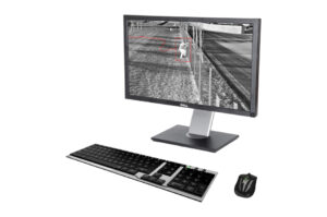Ein Monitor zeigt ein Überwachungsbild in Schwarz-Weiß mit einer markierten Person in einem roten Kasten, daneben befinden sich eine Tastatur und eine Maus.