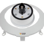 Ein weißer kreisförmiger Kunststoffanschluss mit einem schwarzen Kabelport und der Beschriftung "Axis Communications".