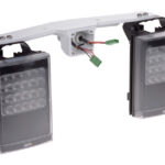 Zwei rechteckige LED-Strahler mit schwarzem Gehäuse, montiert auf einem weißen Halter mit herausragenden Kabeln.