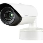 Eine weiße Überwachungskamera mit schwarzem Objektiv, montiert auf einem drehbaren Sockel.