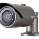 Eine graue Überwachungskamera mit dem Logo "Wisenet" auf der Seite, montiert auf einem runden Sockel.