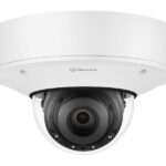 Eine Überwachungskamera im weißen Gehäuse mit transparentem Schutz und sichtbarem Objektiv.