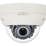 Eine weiße Überwachungskamera von Wisenet in einer kuppelförmigen Ausführung mit sichtbarem Kameraobjektiv im Inneren.