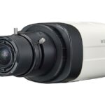 Eine Sicherheitskamera mit einem weißen Gehäuse und einem großen schwarzen Objektivaufsatz. Auf der Seite ist der Schriftzug "Wisenet" zu sehen.