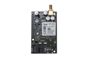 Ein elektronisches Modul mit der Aufschrift "Telit GE910-QUAD", mehreren Kondensatoren und einem goldfarbenen Anschluss oben.