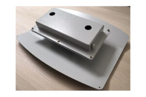 Ein grauer Metallkasten mit zwei Löchern auf einer rechteckigen Basis, auf einem Holztisch platziert.