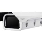 Eine weiße Sicherheitskamera mit rechteckigem Gehäuse und Schutzabdeckung.