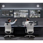 Zwei Personen sitzen vor mehreren Bildschirmen in einem Kontrollraum.