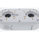 Ein rechteckiges, weißes Gerät mit abgerundeten Ecken, das zwei runde Vertiefungen mit mehreren elektrischen Kontakten auf der Oberseite aufweist.