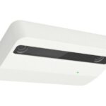 Ein weißer, rechteckiger Sensor mit abgerundeten Kanten und schwarzem Sichtfenster, an einer Decke installiert.