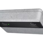 Ein rechteckiger, metallischer Sensor mit zwei Linsen und einem kleinen grünen Licht auf der Vorderseite.