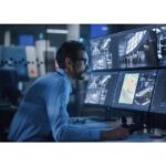 Eine Person überwacht mehrere Überwachungsbildschirme in einem modernen Kontrollraum.