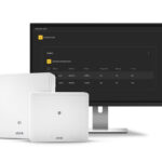 Ein Bildschirm zeigt eine Benutzeroberfläche zur Verwaltung drahtloser Schlösser. Im Vordergrund befinden sich zwei weiße elektronische Geräte mit dem Logo "AXIS".