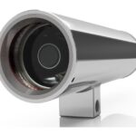 Zylindrische Edelstahlkamera mit schwarzem Glas an der Frontlinse, montiert auf einem rechteckigen Sockel.