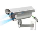 Industriekamera mit robustem Gehäuse und blauem Lichteffekt, montiert an einer Wandhalterung mit grünem Kabel.