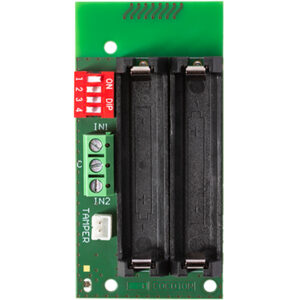 Eine grüne elektronische Leiterplatte mit zwei schwarzen Batteriehalterungen, roten DIP-Schaltern und grünen Schraubklemmen, markiert mit IN1 und IN2.