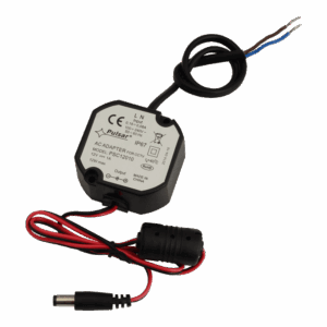 Ein schwarzes AC-Adaptergehäuse der Marke Pulsar, Modell PSC12010, vorgesehen für CCTV-Anwendungen, mit technischen Angaben wie 12V und 1A Ausgang sowie IP67-Schutzniveau. Eine schwarze und eine rote Anschlussleitung sind zu sehen, letztere endet in einem Zylinderstecker.