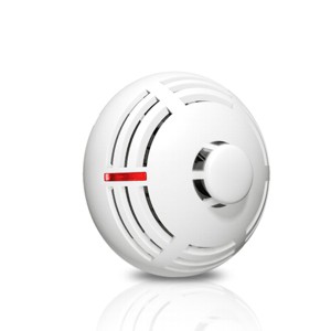 Runder weißer Rauchmelder mit einem kleinen roten Licht auf einer reflektierenden Oberfläche.