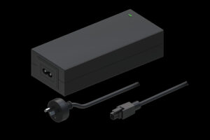 Schwarzes Netzteil mit einem Kabel und Netzstecker, das eine grüne Kontrollleuchte aufweist, auf schwarzem Hintergrund dargestellt.