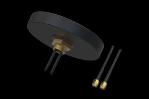 Eine schwarze, runde Antenne mit zwei abgehenden Kabeln und goldenen Anschlüssen auf einem schwarzen Hintergrund.
