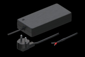 Schwarzes Netzteil mit dreipoligem Stecker und offenem Kabelende vor schwarzem Hintergrund.