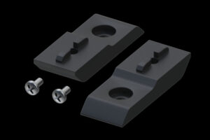 Zwei schwarze Bauteile aus Metall oder Kunststoff mit rechteckiger Form, jeweils mit einer kreisförmigen Vertiefung und einer Erhöhung in der Mitte; daneben zwei silberne Schrauben mit Kreuzschlitz.