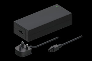 Ein schwarzes Netzteil mit einem britischen Stecker und einem abnehmbaren Stromkabel, auf schwarzem Hintergrund.