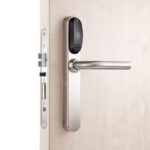 Eine Holztür mit einem modernen, silbernen Türdrücker und einem elektronischen Türschloss mit schwarzem Gehäuse.