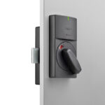 Nahaufnahme eines modernen elektronischen Türschlosses an einer grauen Tür, mit einer dunklen Abdeckung und einem drehbaren Griff.