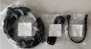Drei Kabel in Plastikbeuteln nebeneinander auf einer Oberfläche. Kabel 1 ist ein großes, aufgerolltes Kabel mit einer Länge von 10 Metern. Kabel 2 ist ein langes, dünneres Kabel mit einer Länge von 10 Metern. Kabel 3 ist ein kürzeres Kabel mit einer Länge von 0,37 Metern. Jedes Kabel hat ein Etikett mit Beschreibung und Längenangabe.
