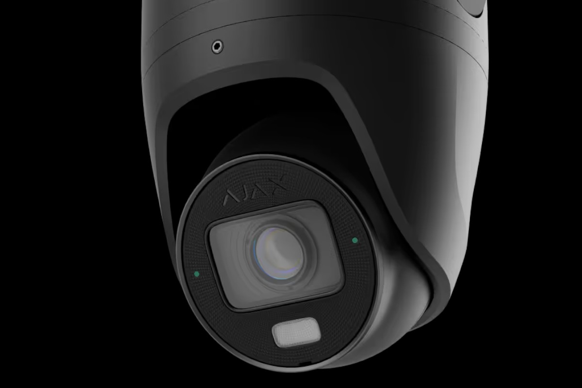 Nahaufnahme einer modernen schwarzen Überwachungskamera mit der Aufschrift "AJAX" auf dem Objektiv, vor einem schwarzen Hintergrund.