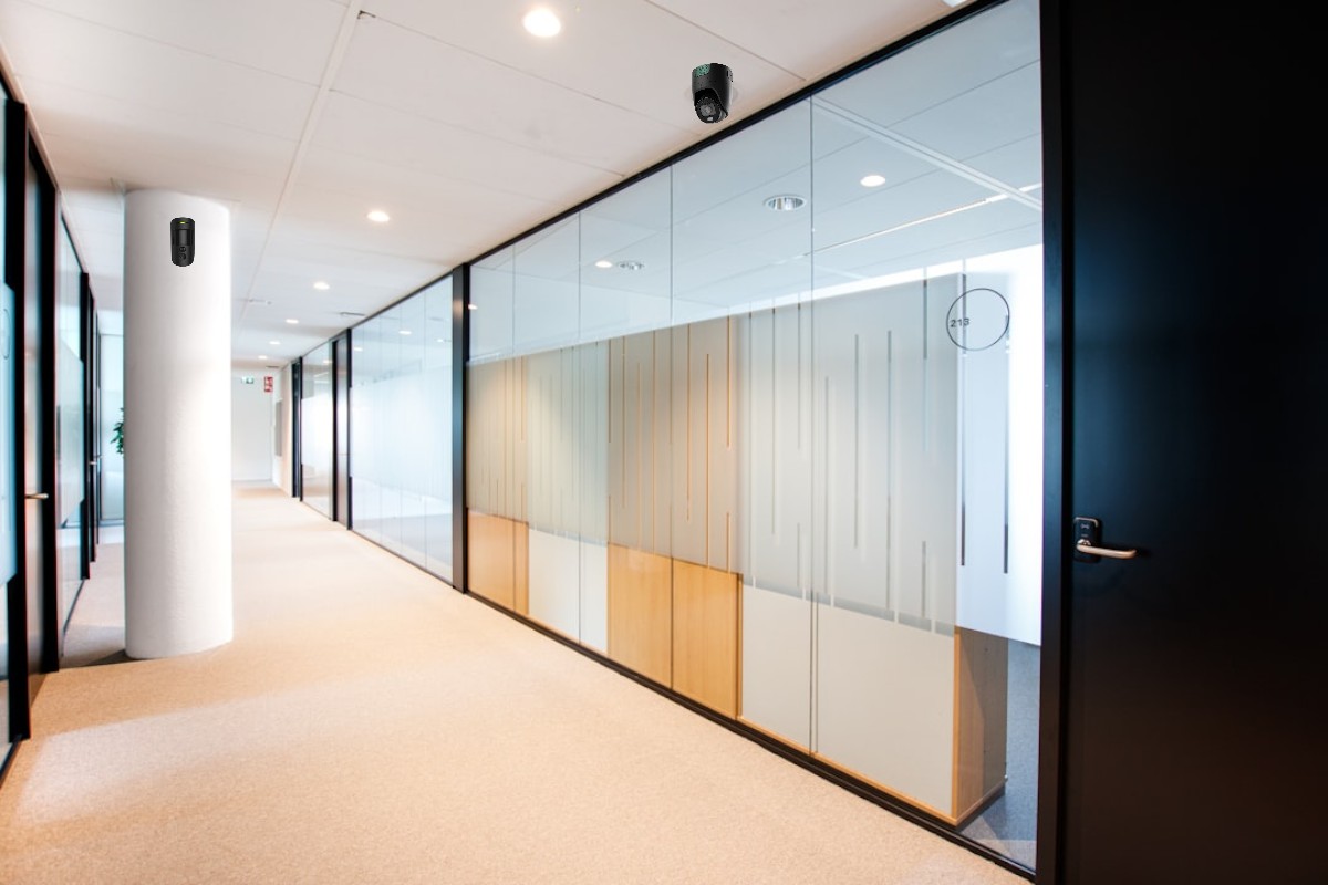 Ein moderner Büroflur mit Glaswänden, die verschiedene Büroräume trennen; die Wände sind mit vertikalen Streifen verziert, und die Decke ist mit eingebauten Leuchten ausgestattet.