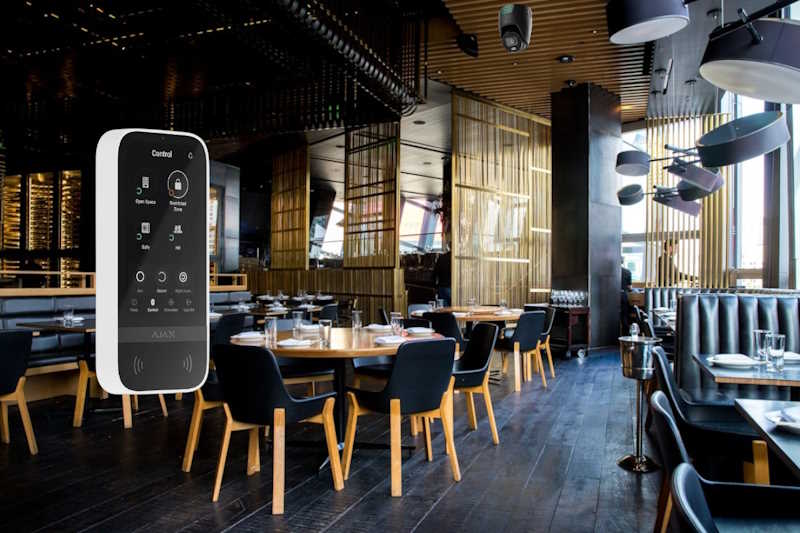 Ein modernes Restaurant mit Holztischen und schwarzen Stühlen, daneben schwebt ein digitales Steuergerät mit einem Touchscreen-Display.