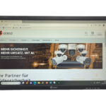 Ein Monitor zeigt eine Webseite von eneo mit Werbematerial für Überwachungskameras und dem Slogan "Mehr Sicherheit. Mehr Umsatz. Mit AI".