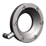 Ein rundes Maschinenteil mit Schrauben und einem seitlichen Anschluss.