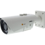 Weiße Überwachungskamera mit Linsenschutz, an der Wand montiert.