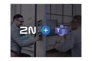 Ein Mann interagiert mit einem Türsystem neben einem großen "2N + T"-Logo; ein anderer Mann sitzt an einem Computer.