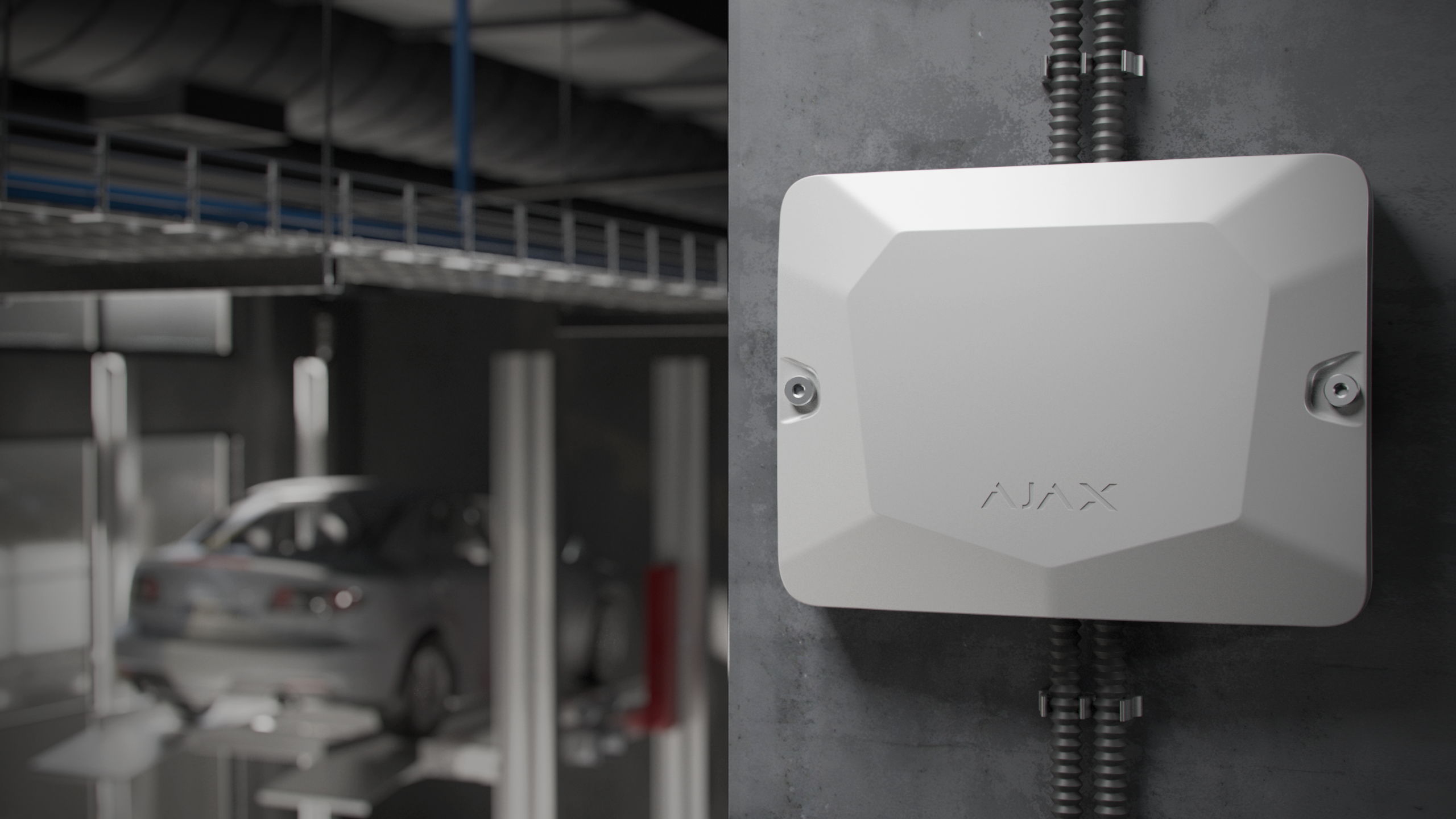 Ein weißes Ajax-Gerät an einer Betonwand in einer Autowerkstatt mit einem angehobenen Auto im Hintergrund.