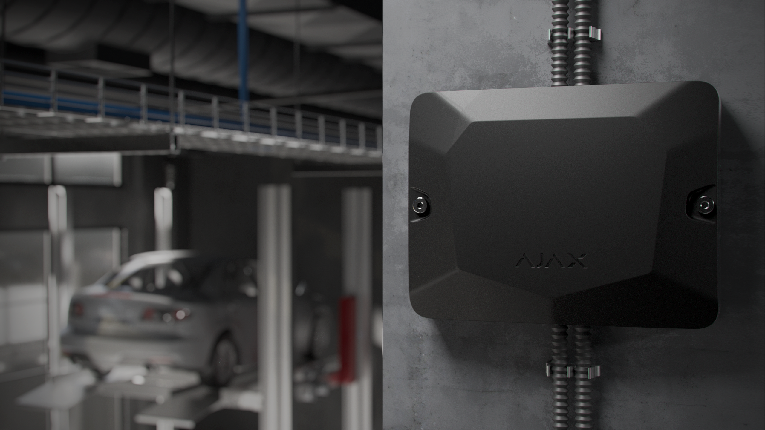 Schwarzes Gerät an einer grauen Wand in einer Werkstatt mit einem Auto auf einer Hebebühne im Hintergrund.