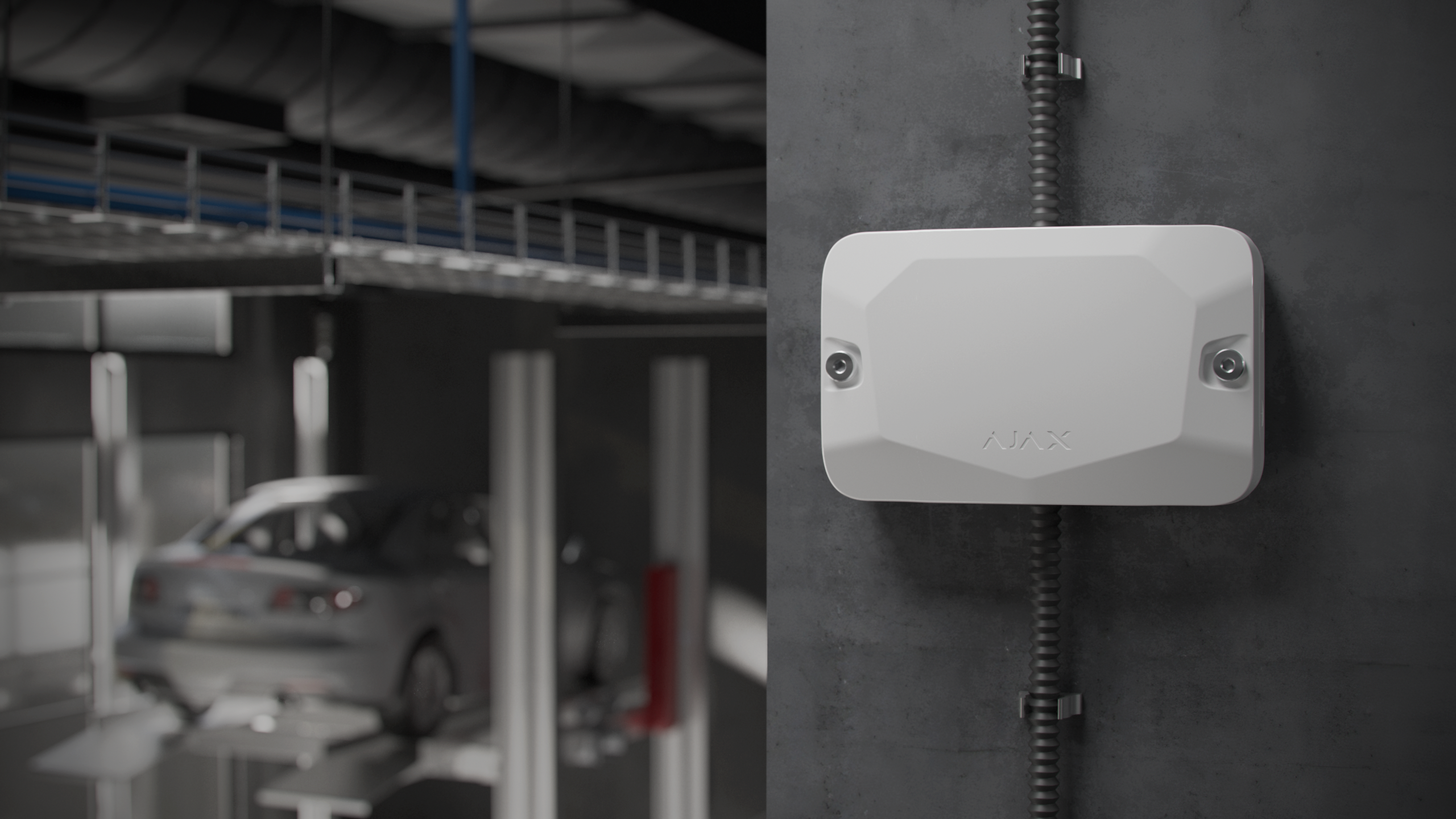 Ein weißes Gerät ist an einer grauen Wand in einer Werkstatt montiert; im Hintergrund steht ein Auto auf einer Hebebühne.