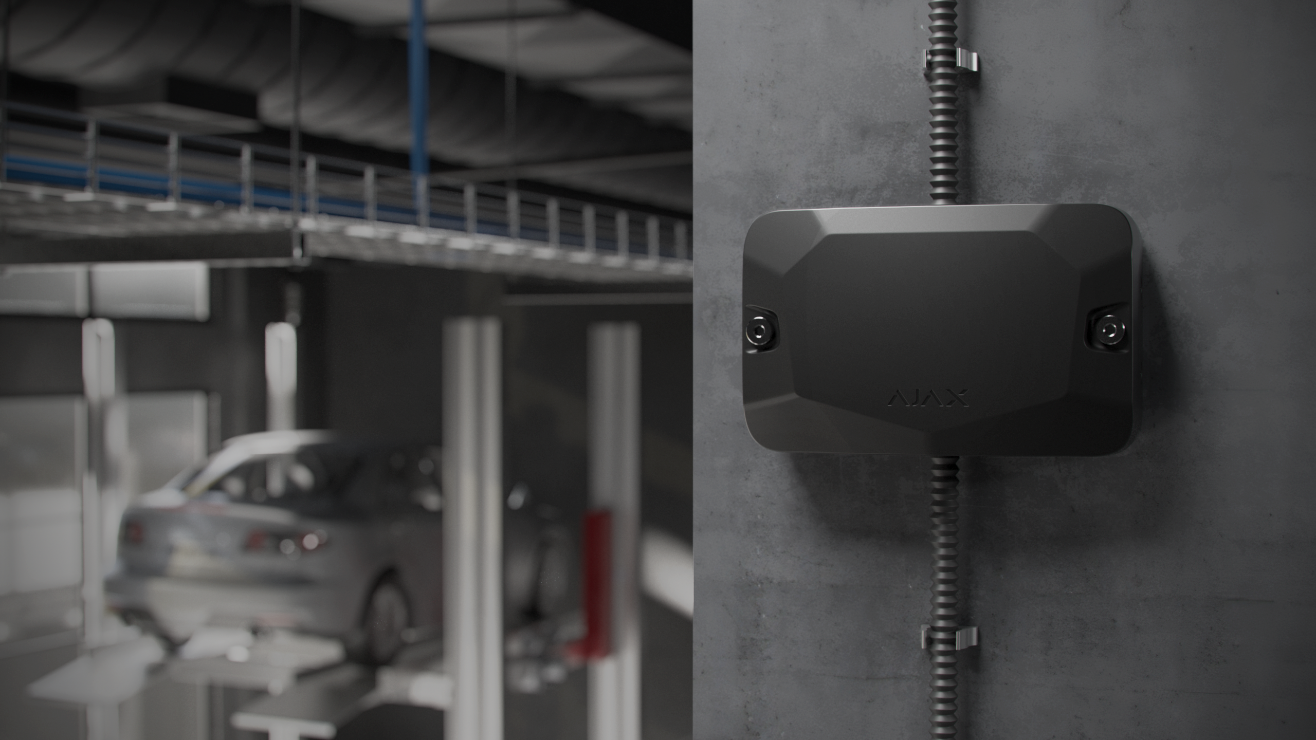 Ein schwarzes Gerät ist an einer Wand in einer Werkstatt montiert, während ein Auto auf einer Hebebühne im Hintergrund steht.