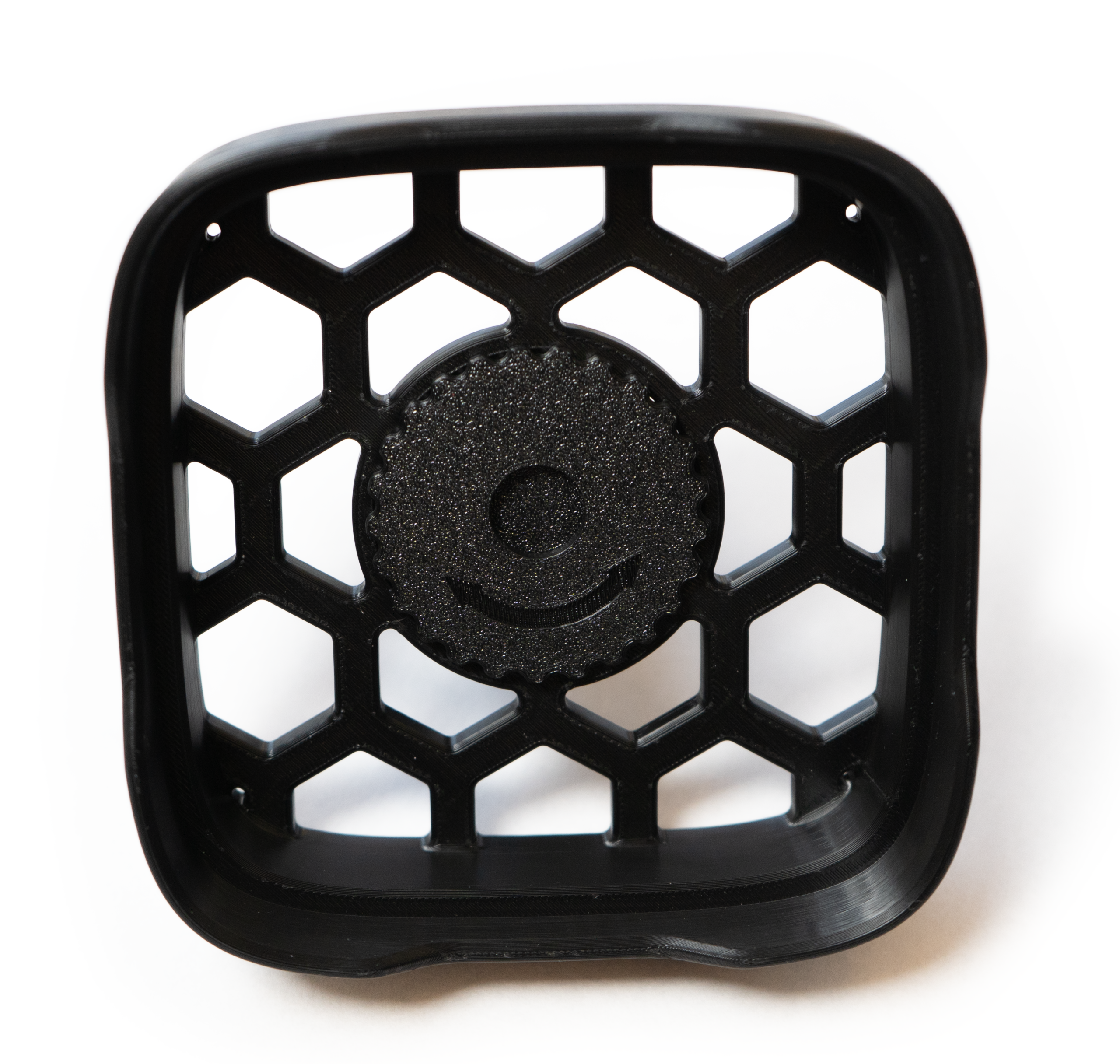 Schwarzes, quadratisches Gitter mit Wabenmuster und rundem mittleren Emblem auf weißem Hintergrund.