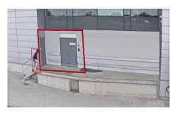 Eine Person verlässt ein Gebäude durch eine Tür auf einer erhöhten Plattform, umgeben von roten Umrisslinien.